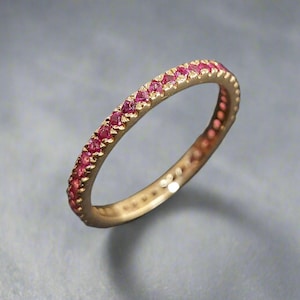 Könnte beinhalten: Ein Goldring mit einer Reihe kleiner rosafarbener Edelsteine, die um die gesamte Band gefasst sind.