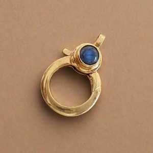 Puede incluir: Un cierre de langosta dorado con un cuerpo redondo y una pequeña piedra preciosa azul engastada en la parte superior. El cierre está diseñado para la fabricación de joyas y presenta un mecanismo de cierre seguro.