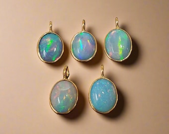 May include: Five oval opal pendants with gold-colored settings. The opals display a range of colors, including blue, green, and flashes of iridescent light. The pendants are arranged on a neutral-toned background, showcasing the jewelry.