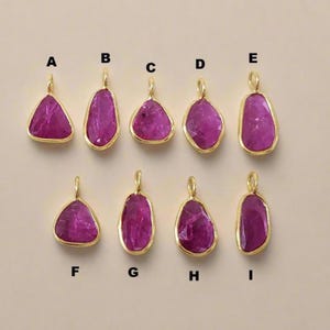 May include: Nine ruby pendants with gold-coloured bezels. The pendants vary in shape, including triangular, oval, and irregular forms. Each pendant has a loop at the top for a chain or cord.