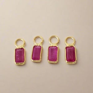 May include: Four gold-toned rectangular charms with a vibrant magenta-colored stone center. Each charm has a small loop at the top for attachment. The charms are displayed on a neutral background.