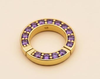 May include: A gold-colored ring with a circular design. The ring is adorned with small, round, purple gemstones set around the outer edge. The number "10" is engraved on the inside of the ring.