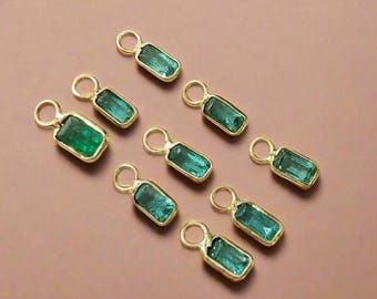 May include: A collection of nine gold-colored pendants, each featuring a rectangular, emerald-green gemstone. The gemstones are set in a gold bezel and have a small loop at the top for attaching to a chain or other jewelry component. The pendants are displayed on a neutral background.