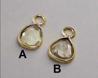 May include: Two gold-toned pendants with clear faceted gemstones. The pendants have a small loop at the top for attaching to a chain or cord. The pendant on the left is labeled "A" and the pendant on the right is labeled "B".