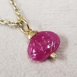 May include: A pink carved ruby pendant with a small diamond accent on a gold chain.