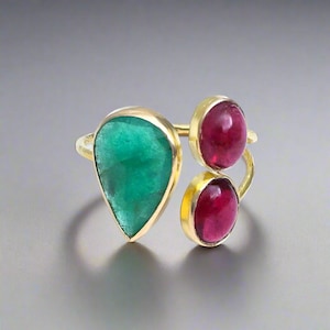 May include: A gold ring with a green emerald gemstone and two pink ruby gemstones.