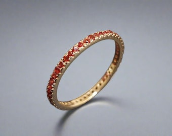 May include: A gold band ring with a row of small, orange gemstones set around the entire band.