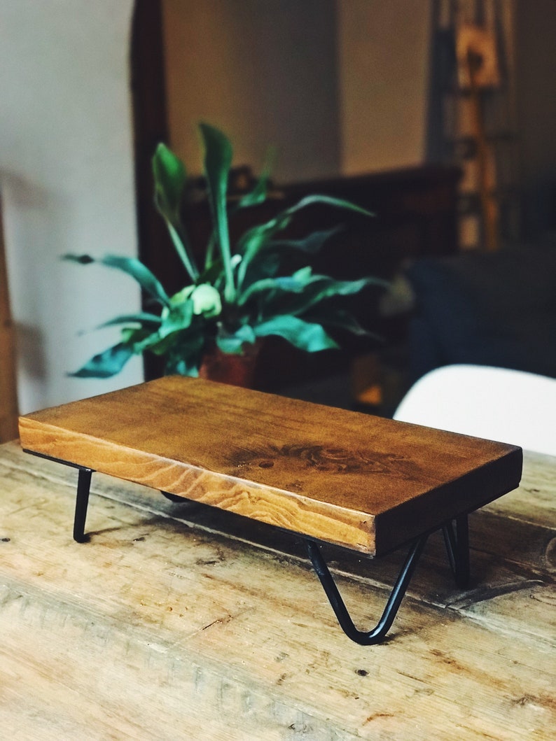 Op de afbeelding: Een houten plank met zwarte metalen poten. De plank is gemaakt van natuurlijk hout en heeft een rustieke uitstraling. De plank staat op een houten tafel.
