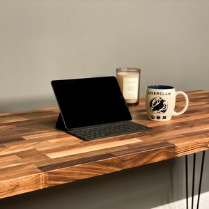 May include: A wooden desk with a black laptop, a white mug with the words "Ravenclaw" and a black bird design, and a glass candle holder.