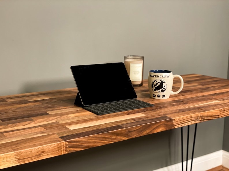 May include: A wooden desk with a black laptop, a white mug with the words "Ravenclaw" and a black bird design, and a glass candle holder.