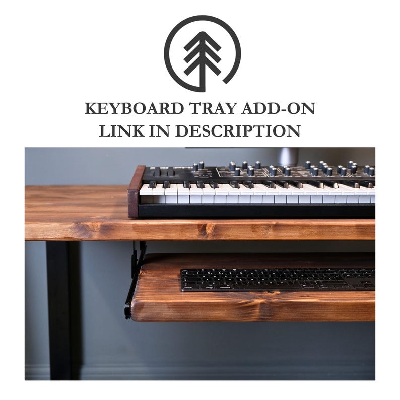 A wooden desk with a sliding keyboard tray. The desk is made of dark wood and has a black metal frame. The keyboard tray is made of the same wood and is attached to the underside of the desk. A black keyboard is on the tray. A black synthesizer is on the desk.