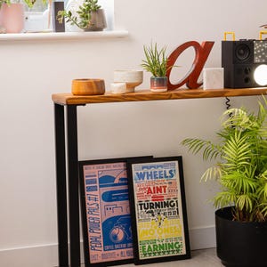 Wooden console table with black square metal legs, styled as a radiator shelf in a modern hallway with plants, books, and decorative objects on top.