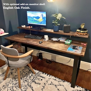 Solid wood desk with monitor shelf and black steel legs. Dark wood colour and placed in a dark coloured wall room with a warm industrial feel.
