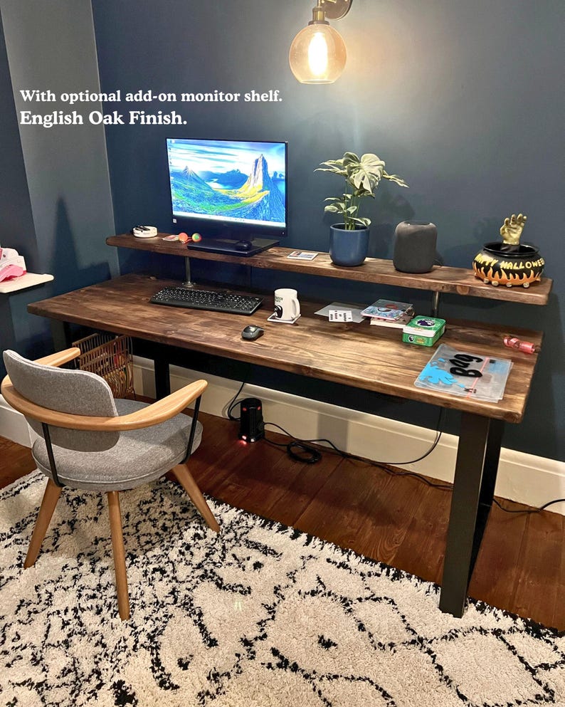 Solid wood desk with monitor shelf and black steel legs. Dark wood colour and placed in a dark coloured wall room with a warm industrial feel.