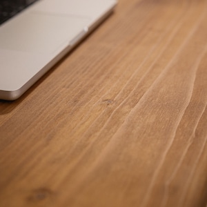 Close up of solid wood desk surface showing natural grain detail with a laptop resting on top.