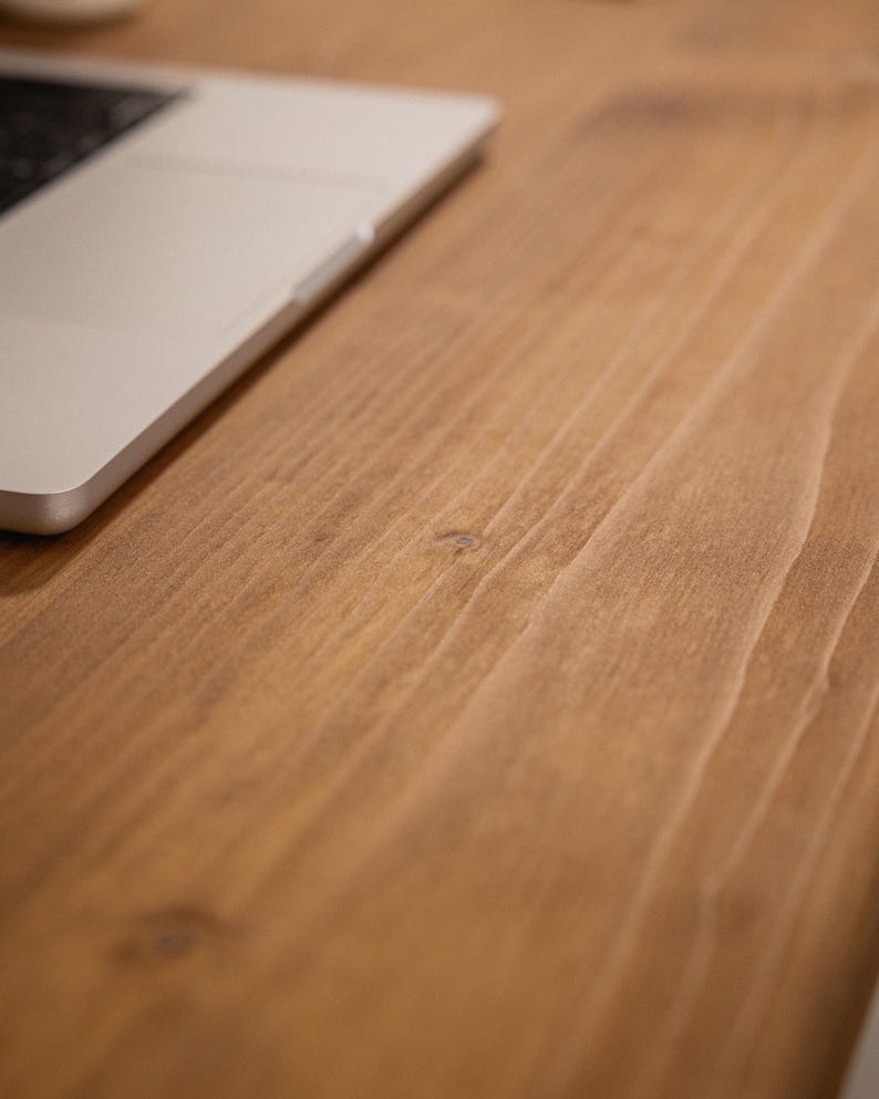 Close up of solid wood desk surface showing natural grain detail with a laptop resting on top.