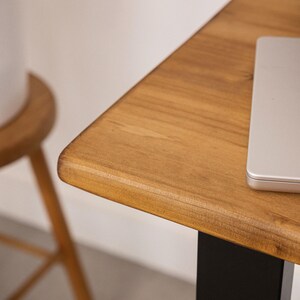 Close up of solid wood desk corner with rounded edge and natural grain, with laptop partially visible.