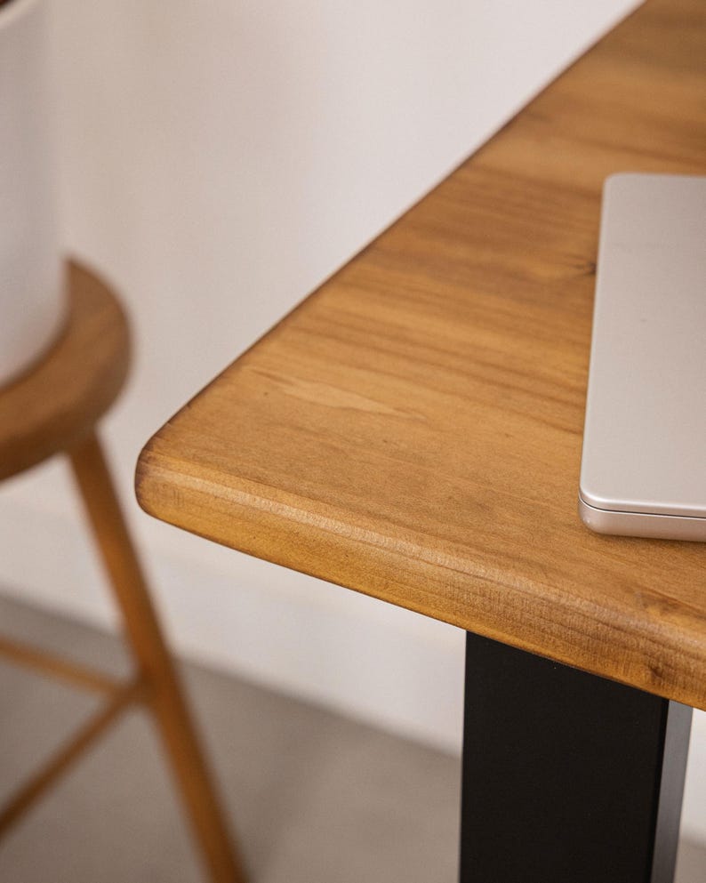 Close up of solid wood desk corner with rounded edge and natural grain, with laptop partially visible.