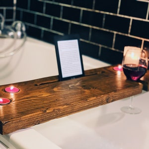 Peut inclure: Un plateau de bain en bois avec un lecteur de livres, deux bougies roses et un verre de vin rouge. Le plateau est placé sur une baignoire blanche.