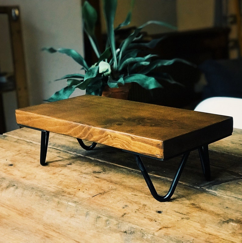 Op de afbeelding: Een houten plank met zwarte metalen poten. De plank is gemaakt van natuurlijk hout en heeft een rustieke uitstraling. De plank staat op een houten tafel.