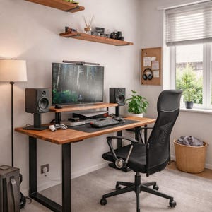 Pode incluir: Uma configuração moderna de escritório doméstico com uma secretária de madeira com pernas de metal preto, uma cadeira ergonómica preta e um monitor grande. A secretária está equipada com colunas, um teclado e um rato. Duas prateleiras de madeira estão montadas na parede acima da secretária.