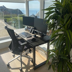 Solid wood desk with a black finish and black steel legs. Placed in a bright room with large windows, overlooking cliffs and the sea.