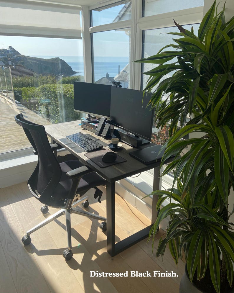 Solid wood desk with a black finish and black steel legs. Placed in a bright room with large windows, overlooking cliffs and the sea.