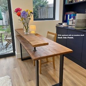 Solid wooden desk with a medium to dark finish and black steel legs. It features an optional monitor shelf add-on and it's styled with a vase of flowers.