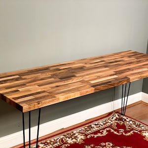 May include: A wooden desk with a natural wood finish and black hairpin legs. The desk is made of multiple pieces of wood that are arranged in a parquet pattern.