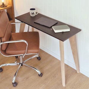 Op de afbeelding: Een moderne thuiskantooropstelling met een donkerbruine bureau met licht houten poten. Een bruine leren bureaustoel staat voor het bureau. Een laptop, notitieboek en een mok met de tekst "Ravenclaw" liggen op het bureau.