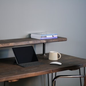 K&ouml;nnte beinhalten: Ein dunkelbrauner Holzschreibtisch mit einem Metallgestell und einem oberen Regal. Auf dem Schreibtisch befinden sich ein Laptop, eine Tastatur, eine Maus, eine Tasse und eine Kerze. Auf dem oberen Regal steht ein kleiner Topf mit einem Kaktus.