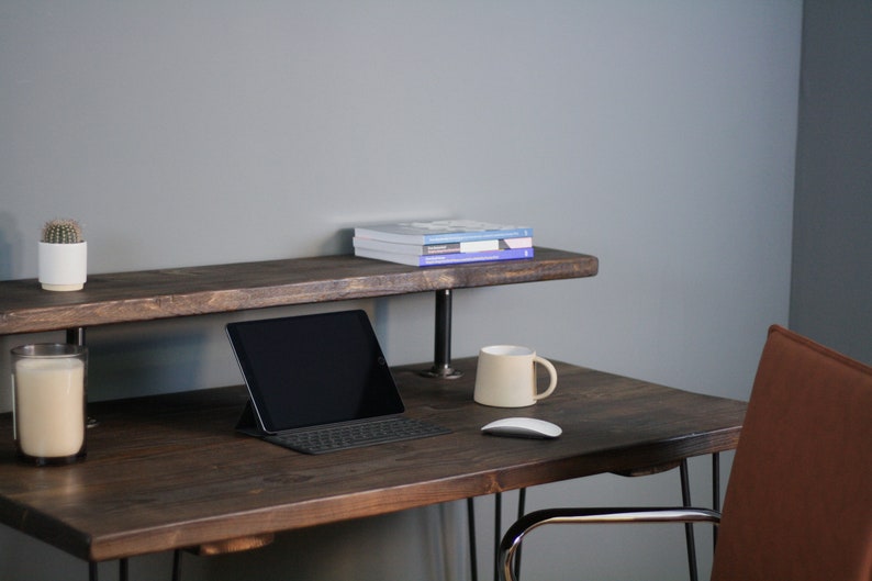 K&ouml;nnte beinhalten: Ein dunkelbrauner Holzschreibtisch mit einem Metallgestell und einem oberen Regal. Auf dem Schreibtisch befinden sich ein Laptop, eine Tastatur, eine Maus, eine Tasse und eine Kerze. Auf dem oberen Regal steht ein kleiner Topf mit einem Kaktus.