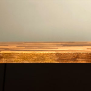 May include: A close-up of a wooden table top with a light brown finish. The table top is made of multiple pieces of wood that are arranged in a checkered pattern. The table top is in focus, while the background is blurred.