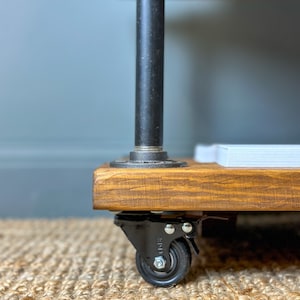 Puede incluir: Una estanter&iacute;a de madera con patas de tubo de metal negro y ruedas negras. La estanter&iacute;a est&aacute; te&ntilde;ida de un color marr&oacute;n oscuro y tiene una pila de papel blanco en la parte superior.