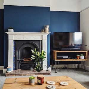 May include: A living room with a dark blue wall, a white fireplace, a wooden TV stand with hairpin legs, and a wooden coffee table with coasters.