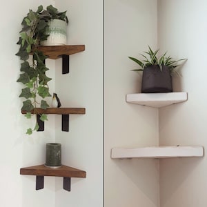 Puede incluir: Dos juegos de estanterías de esquina. Un juego presenta tres estantes de madera con soportes de metal negro, que exhiben una planta en maceta, un pájaro decorativo y una vela. El otro juego tiene dos estantes blancos con una planta en maceta.