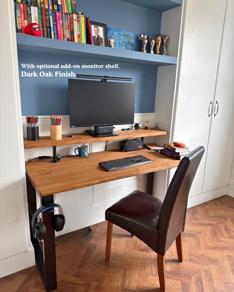 Solid wood desk with a monitor shelf, medium to dark wood finish and black steel legs. Placed in a narrow alcove with a few book shelves above it.