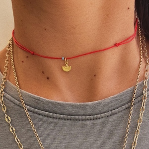 May include: A layered necklace set featuring a red cord choker with a gold fan pendant and a turquoise bead. Below, two gold chain necklaces with a flower pendant.