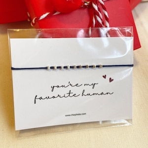 Könnte beinhalten: Ein blaues Armband aus Schnur mit silbernen Perlen und dem Text "you're my favorite human" auf einer weißen Karte mit einem roten Herzen.