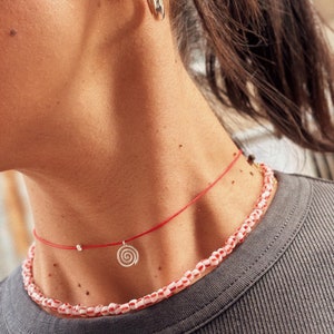 May include: A red string choker necklace with a silver spiral charm and a white and red beaded necklace layered on top.