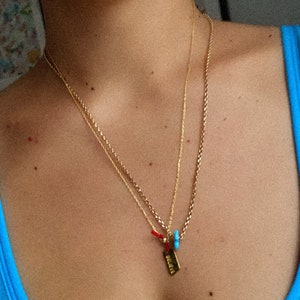 May include: A gold chain necklace with three pendants. The pendants are a small turquoise bead, a red string, and a gold tag that says "Believe".