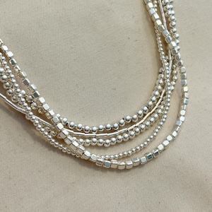 May include: A silver multi-strand necklace with round and square beads.