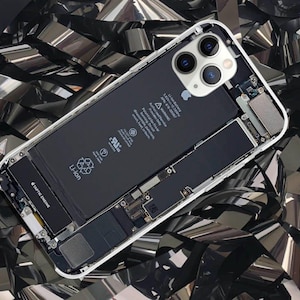 May include: A white iPhone with a clear back panel revealing the internal components, including the battery, motherboard, and camera system. The phone is lying on a bed of silver and black metallic confetti.