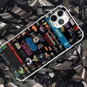 May include: A clear phone case displaying a collection of iconic VHS movie covers, such as "Blade Runner," "Star Wars," and "Back to the Future." The case has a white border and a multi-lens camera cutout. The background is a reflective, metallic material.