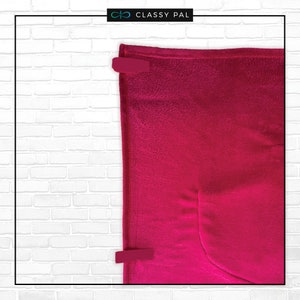May include: A bright pink fleece blanket with a pocket on the bottom right corner. The blanket is folded and secured with two red clips.