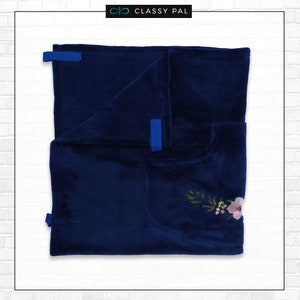 Puede incluir: Una manta de forro polar azul marino con un dise&ntilde;o de bordado floral y lazos de cinta azul.