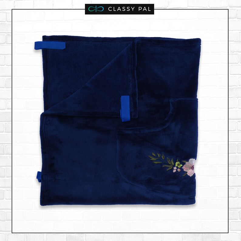 Puede incluir: Una manta de forro polar azul marino con un dise&ntilde;o de bordado floral y lazos de cinta azul.