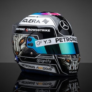 Può includere: Un casco da corsa nero con una grafica di tigre bianca dagli occhi arancioni luminosi sui lati. Il casco presenta i loghi Mercedes, Crowdstrike, G42, Y.3, Petronas, Signify, Akkodis e WhatsApp, con una visiera dai riflessi blu.