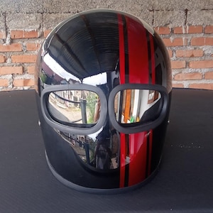 May include: A glossy black full-face motorcycle helmet featuring a prominent vertical red racing stripe running down the center. The helmet includes two distinct, separate eye ports with reflective, mirrored lenses and a matte black trim border.