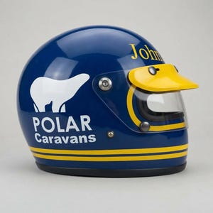May include: A dark blue full-face helmet featuring a white polar bear graphic and the text "POLAR Caravans" on the side. The helmet includes a yellow visor peak, a clear face shield, and two horizontal yellow stripes running along the base.